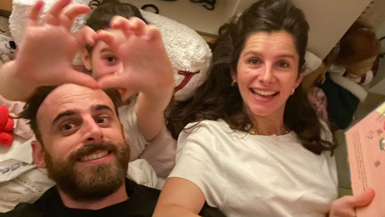Papa, maman et Bianca, allongés et souriants, Bianca fait un cœur avec ses mains